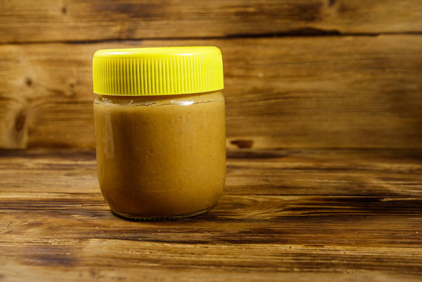 Jar of peanut butter on a wooden table - Zdjęcie, obraz