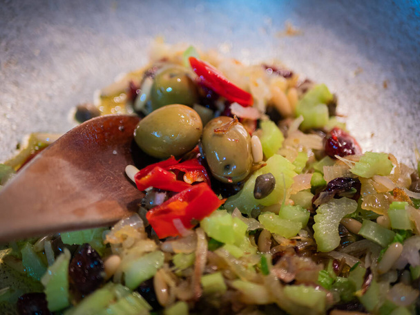 Κοντινό πλάνο ενός καρυκεύματος φυτικής προέλευσης για τη διάσημη ιταλική συνταγή alla ghiotta. Ντομάτα, σταφίδες, κουκουνάρια, σέλινο, κόκκινο κρεμμύδι, λάδι και πιπέρι. - Φωτογραφία, εικόνα