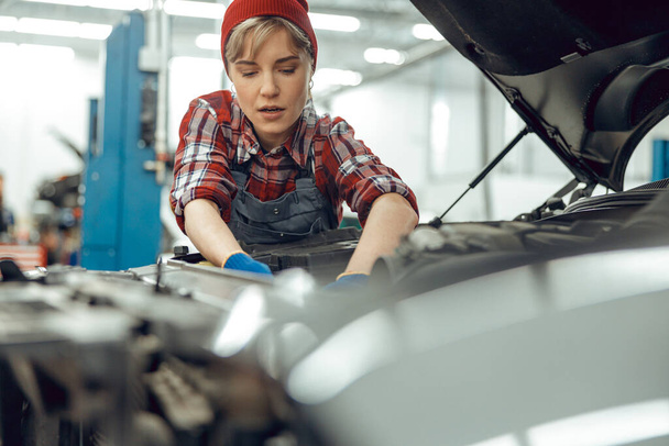 Focused female mechanic checking a car engine - Fotoğraf, Görsel