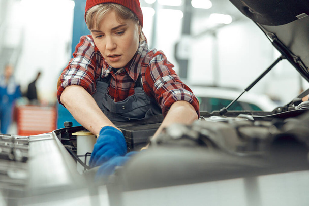Vakava nuori nainen korjaamassa moottoriajoneuvoa
 - Valokuva, kuva
