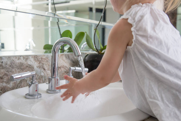 Yıkama - 2 yaşında, sevimli beyaz bir kız ellerini banyo lavabosunda yıkıyor. Eğer erken yaşta öğretmeye başlarsan, el yıkama ömür boyu sağlıklı bir alışkanlık haline gelebilir.. - Fotoğraf, Görsel