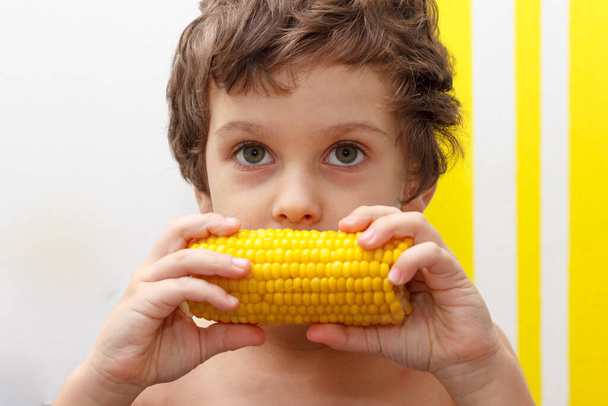 encantador chico rizado comer una mazorca de maíz hervido, OGM gratis
 - Foto, Imagen