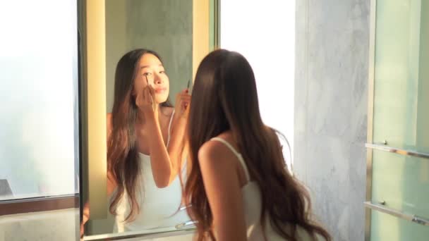 Portret piękna młoda azjatycka kobieta stosowania kosmetyków przez lustro wnętrza łazienki - Materiał filmowy, wideo
