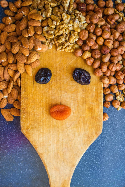 The girl is made of hazelnut, almond, walnut, dried apricots and prunes. Background - vintage cutting board, kitchen utensils. Dietary menu, proper nutrition. - Photo, Image
