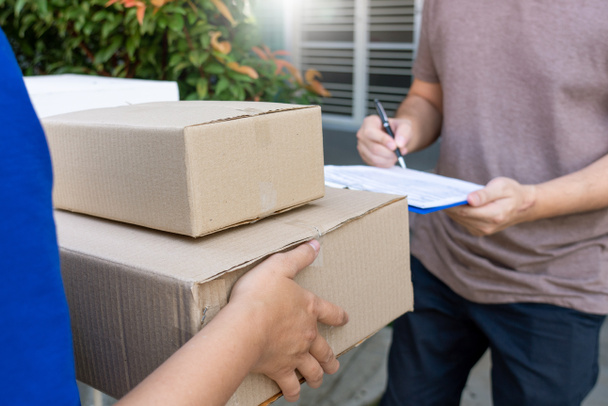Entrega hombre en azul uniforme entrega caja de paquete para la firma del cliente lista de verificación después de confirmar la recepción del paquete
  - Foto, imagen
