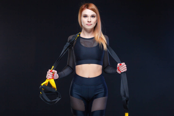 Belle femme de fitness posant avec des sangles de fitness trx dans des vêtements de sport sexy isolés sur fond noir
 - Photo, image