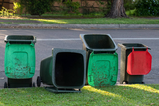 Australische Mülltonnen bleiben stehen und liegen nach der Stadtratssitzung auf einer Straßenseite. Grüne Deckel sind für grüne Gartenabfälle und rote Deckel für allgemeinen Hausmüll - Foto, Bild