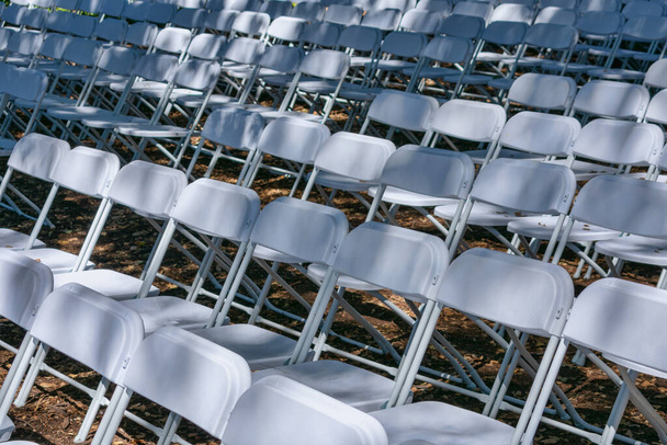 White plastic chairs set up an outdoor in a row before ceremony, event or party. - Valokuva, kuva