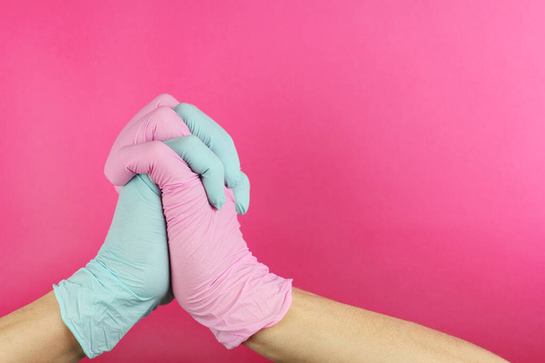 hands in latex medical gloves different color are folded in gesture of supplication, people pray for health in virus epidemic, copy space pink background   - Photo, image