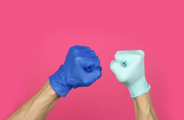 ręce w gumowych rękawiczkach medycznych różnych kolorów zaciśnięty w pięści, oznaka wspólnej walki z epidemią wirusa lub przeciwności losu, zapobieganie i ochrona, kopiowanie przestrzeni różowy tło   - Zdjęcie, obraz