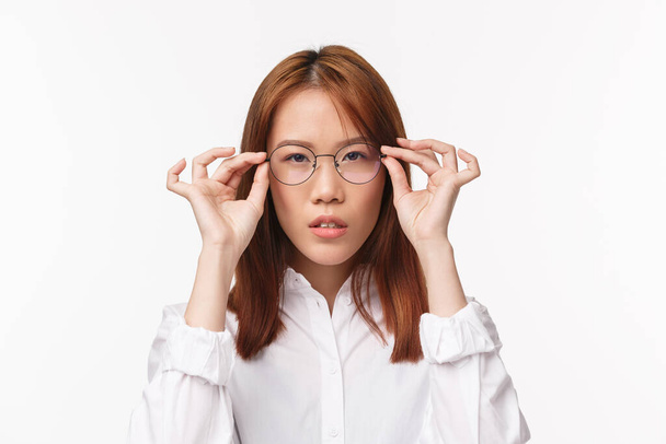 Nahaufnahme Porträt einer seriös aussehenden jungen asiatischen Geschäftsfrau, die eine neue vorgeschriebene Brille anprobiert, sich um das Sehen kümmert, als Pickbrille für die Arbeit mit dem Computer, weißer Hintergrund stehend - Foto, Bild