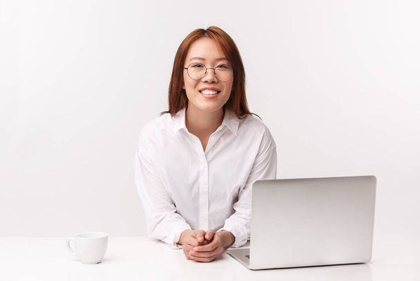 Career, work and women entrepreneurs concept. Close-up portrait of cheerful young businesswoman sitting in office, lean table with laptop, drinking coffee, answer customer questions - Photo, Image