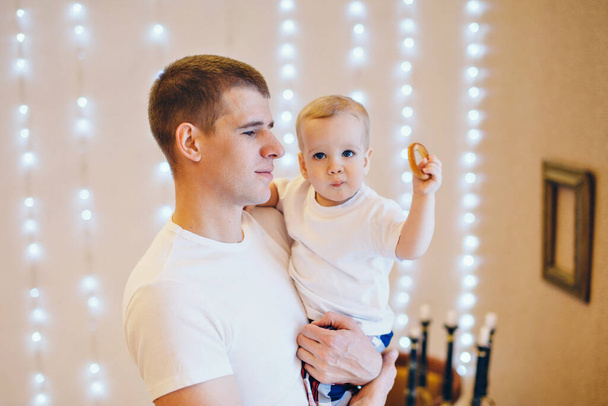 Dad holds the baby in his arms. Boy eating bagel. The concept of educating the father of young children, Happy childhood, a friendly family. - 写真・画像