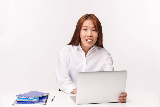 Career, work and women entrepreneurs concept. Close-up portrait of pretty asian female office manager working with laptop, looking at client as writing down info at computer, white background - Photo, Image