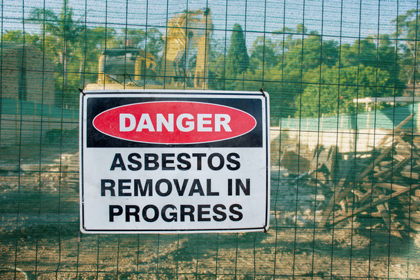 Figyelmeztető jel Veszélyes azbeszt egy kerítésen az építkezésen, ahol a régi ház lerombolja - Fotó, kép