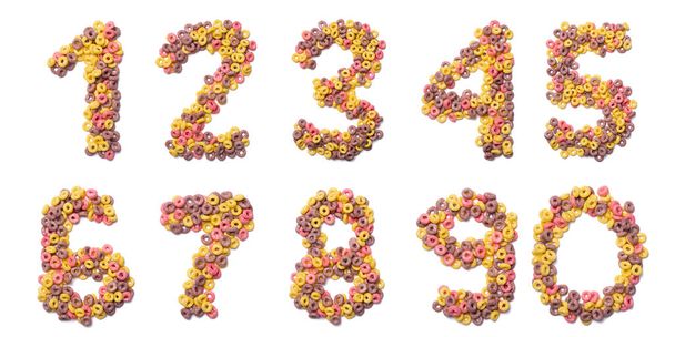 Números arábigos del alfabeto inglés de copos de color rosa sobre un fondo blanco aislado. Patrón alimenticio elaborado con cereales dulces para el desayuno. Alfabeto brillante para tiendas infantiles
.    - Foto, imagen