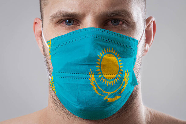 Молодий чоловік з болючими очима в медичній масці, пофарбований в кольори національного прапора Казахстану. Медичний захист від хвороб, що передаються повітрям, коронавірус. Людина боїться підхопити грип. - Фото, зображення