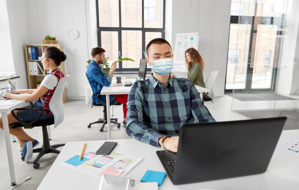 férfi orvosi maszk laptop dolgozik az irodában - Fotó, kép
