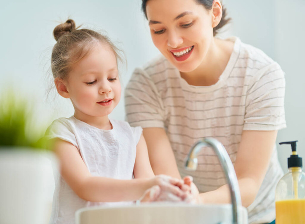 A cute little girl and her mother are washing their hands. Protection against infections and viruses.                                - Foto, afbeelding