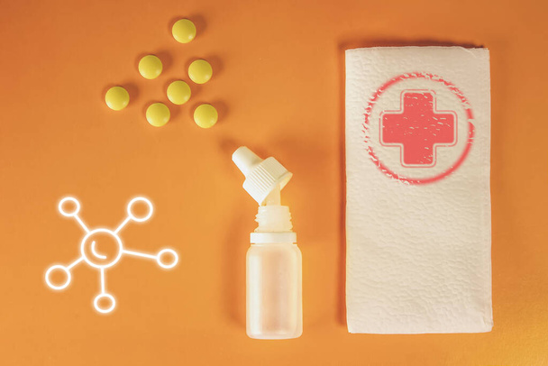 Witte plastic neusspray, tabletten en papieren zakdoeken met het icoon van het medische kruis en het molecuul op oranje achtergrond - sinusitis, geniantritis, rhinitis en andere ziekten van ENT-organen - Foto, afbeelding