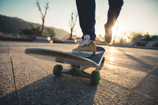 Füße von Skateboarderin beim Sonnenaufgang auf der Straße - Foto, Bild
