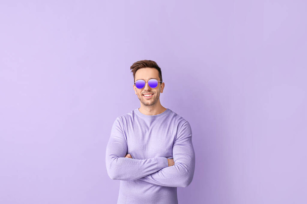 Hombre joven con gafas de sol con estilo en el fondo de color - Foto, imagen