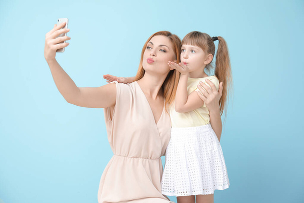Woman and her little daughter taking selfie on color background - Foto, imagen