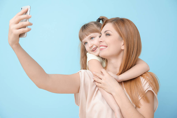 Woman and her little daughter taking selfie on color background - Photo, Image