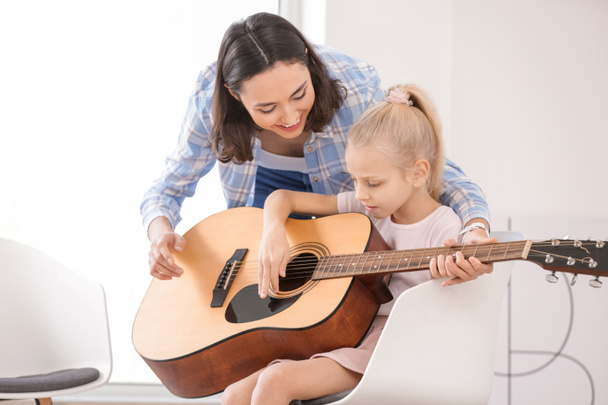 Частный учитель музыки дает уроки гитары маленькой девочке дома
 - Фото, изображение
