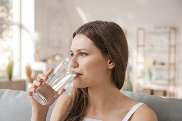 Beautiful young woman drinking water at home - Foto, afbeelding