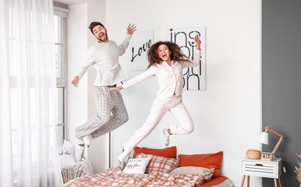 Ευτυχισμένο νεαρό ζευγάρι που πηδάει στο κρεβάτι στο σπίτι - Φωτογραφία, εικόνα