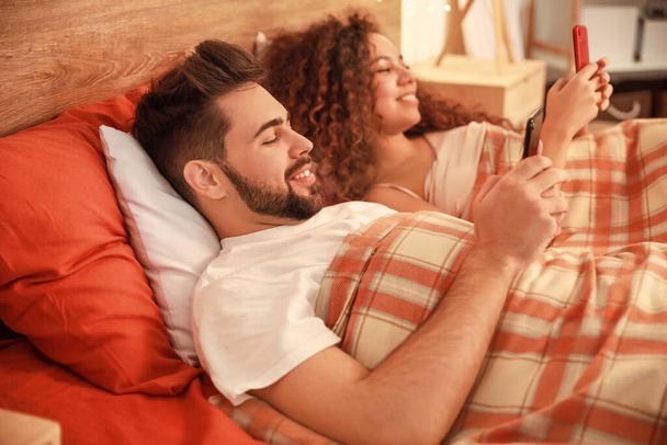 Happy young couple with mobile phones in bedroom - Foto, afbeelding