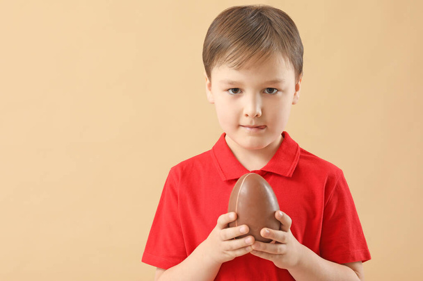 Cute little boy with sweet chocolate egg on color background - Photo, Image