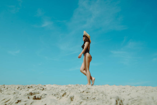 vrouw op zandstrand in zwart badpak blauwe lucht op de achtergrond. zomervakantie - Foto, afbeelding