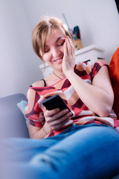 Blond attractive girl is lying on the sofa and texting with her boyfriend - Φωτογραφία, εικόνα