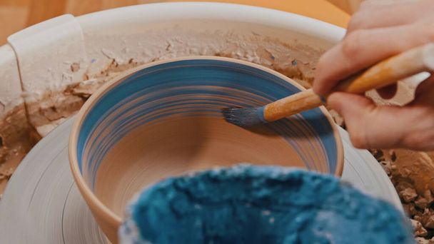 Pottery - člověk maluje hliněnou mísu uvnitř s modrým štětcem na keramické kolo - Fotografie, Obrázek