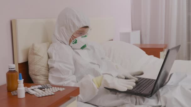 Chłopiec w kombinezonie ochronnym i respirator w domu przy komputerze odizolowanym podczas epidemii. - Materiał filmowy, wideo