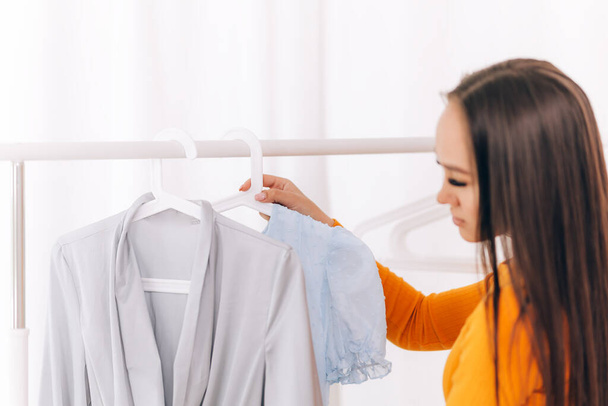 A young girl chooses what clothes to wear, girl looks at clothes in white room - Photo, Image