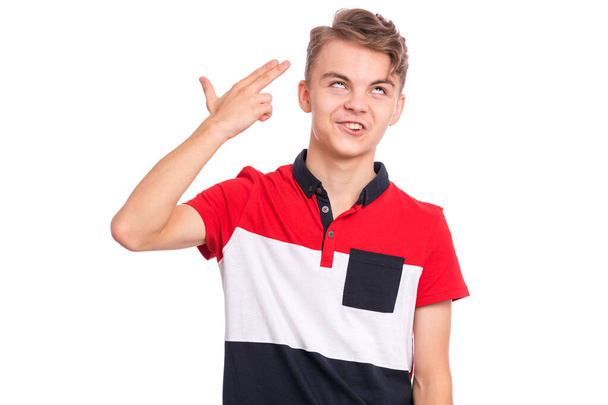 Retrato de um adolescente descontente a fazer um gesto de arma. Adolescente jovem caucasiano apontar os dedos para a cabeça como se ele sobre atirar em si mesmo. Criança segurando arma simbólica isolada no fundo branco
. - Foto, Imagem