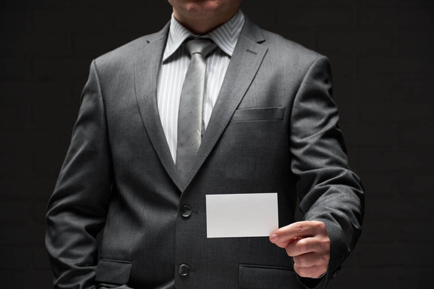 fehér üres névjegykártya közelkép üzletember kezét, szürke öltöny, sötét fal háttér - Fotó, kép