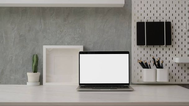 Close-up weergave van moderne werkruimte met blanco beeldscherm laptop, decoraties en kopieerruimte op marmeren bureau met briefpapier op plank met zolderwand  - Foto, afbeelding