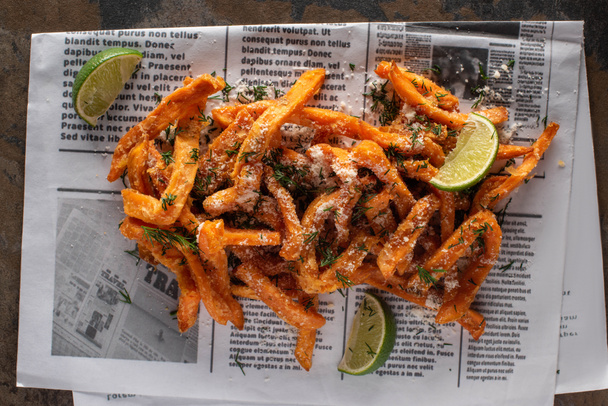 top view of salty french fries and sliced lime on newspaper with text  - Foto, immagini
