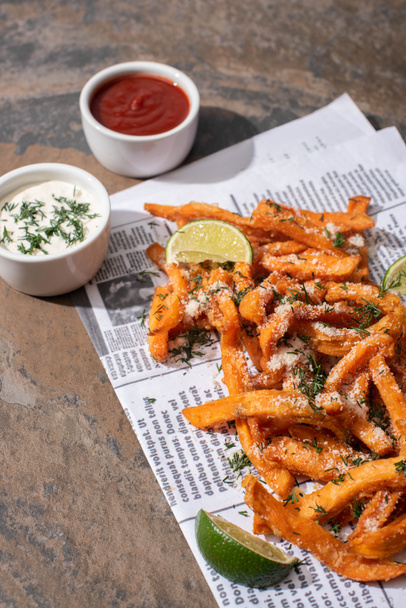 salty french fries, sliced lime, garlic sauce and ketchup on newspaper and marble surface  - 写真・画像