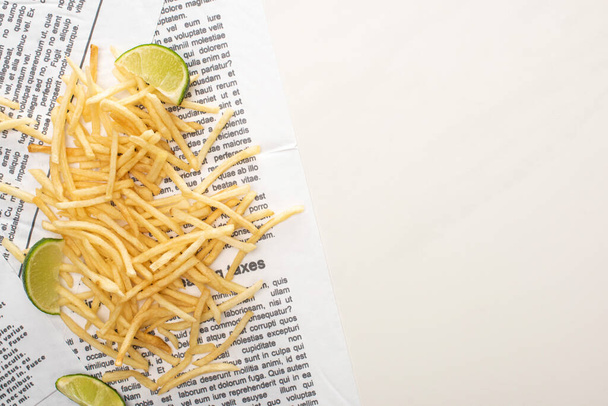 bovenaanzicht van knapperige frietjes en gesneden limoen op krant op wit  - Foto, afbeelding