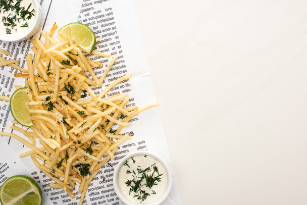 top view of crispy french fries, garlic sauce and sliced lime on newspaper on white  - Photo, Image