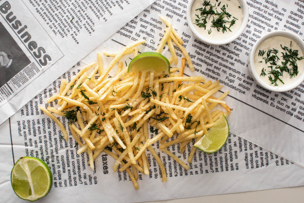 top view of fried french fries, garlic sauce and sliced lime on newspaper - Fotografie, Obrázek