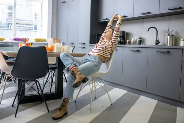 Young woman sitting at the kitchen table, stretching - Foto, Imagen