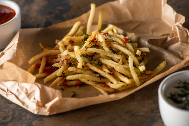 tasty french fries on baking paper near ketchup and garlic sauce on marble surface  - Photo, Image