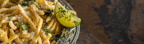 panoramic shot of salted french fries and sliced lime on marble surface  - Foto, Bild