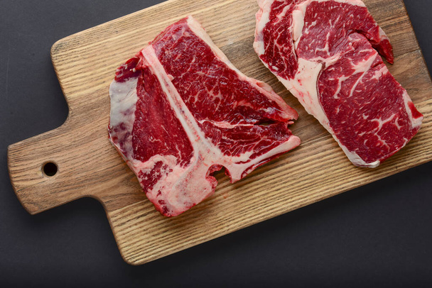 Fresh raw beef steak on wooden cutting board, top view. Served over black background. - Foto, Imagen